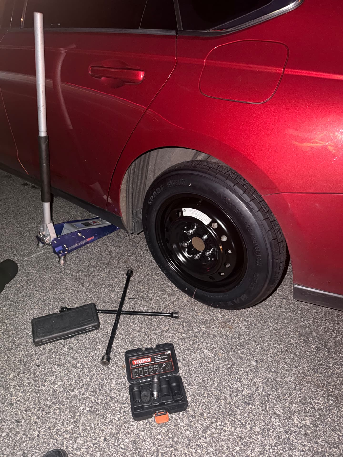 Spare tire installed on a red sedan during a night call